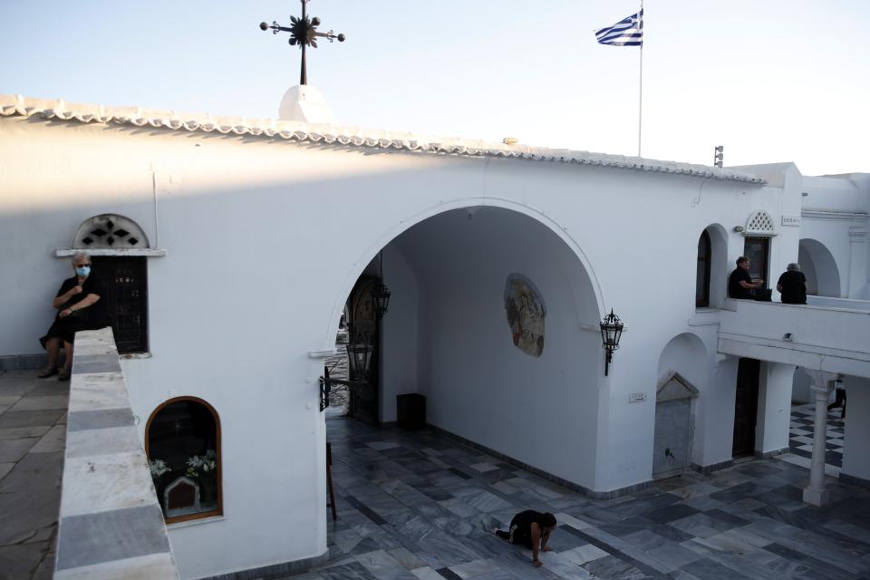 A woman crawls as other pilgrims sit at the yard of the Holy Church of Panagia of Tinos, on the Aegean island of Tinos, Greece, on Thursday, Aug. 13, 2020. For nearly 200 years, Greek Orthodox faithful have flocked to Tinos for the August 15 feast day of the Assumption of the Virgin Mary, the most revered religious holiday in the Orthodox calendar after Easter. But this year there was no procession, the ceremony _ like so many lives across the globe _ upended by the coronavirus pandemic. (AP Photo/Thanassis Stavrakis)