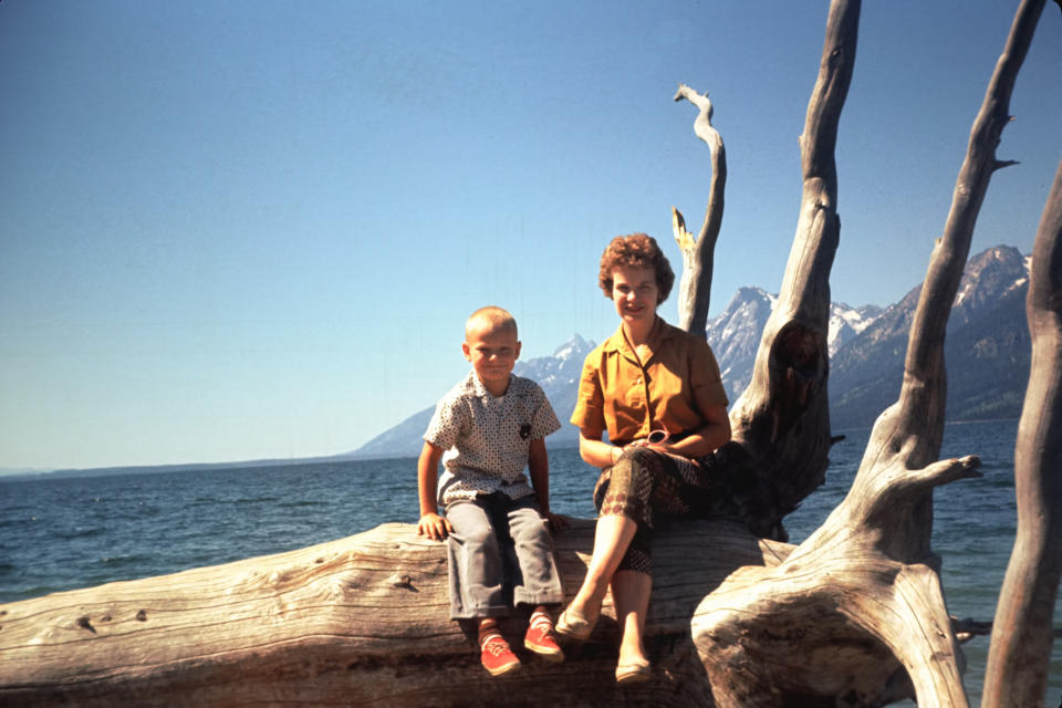 A mother and her son are posing for a picture while sitting on a log