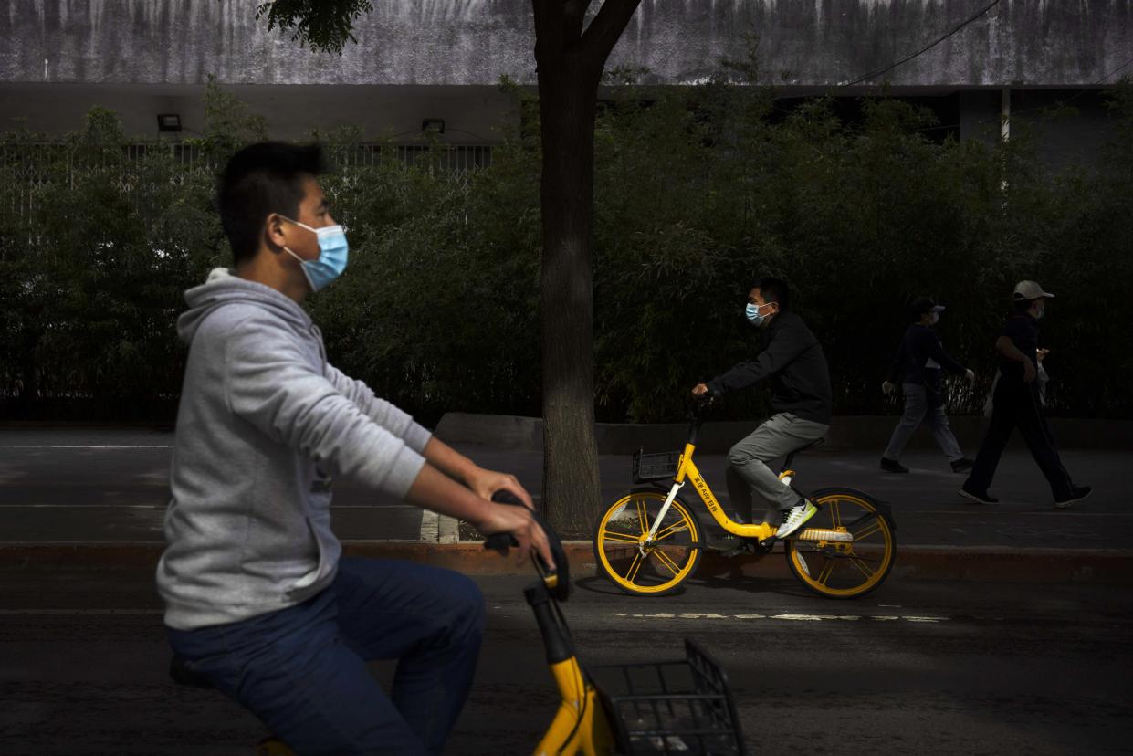 People wearing face masks ride along a street in Beijing on Wednesday.  (Mark Schiefelbein / AP)