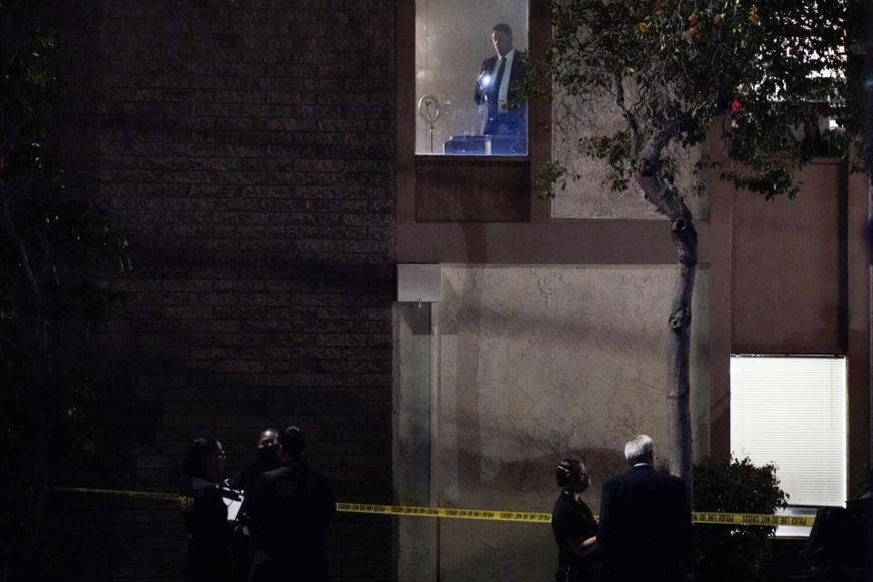 People gather outside a building near yellow police tape.