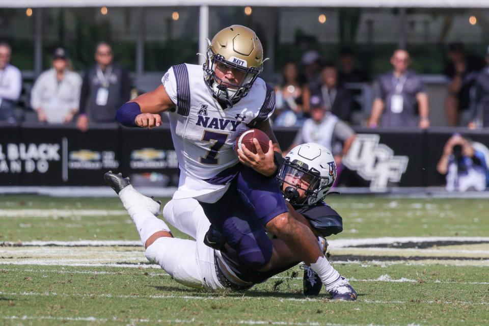 Nov 19, 2022; Orlando, Florida, USA; Navy Midshipmen quarterback Xavier Arline (7) is tackled by UCF Knights linebacker Kam Moore (30) during the second quarter at FBC Mortgage Stadium. Mandatory Credit: Mike Watters-USA TODAY Sports