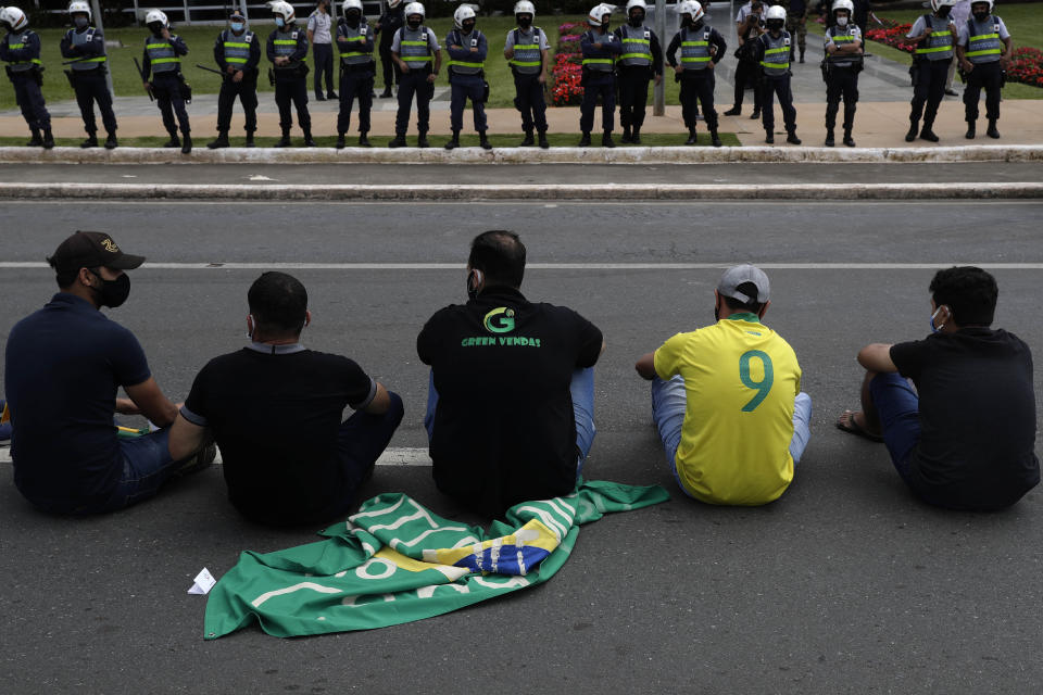 Demonstrators sit in front of police guarding a city government office where they protest a two-week-long lockdown to curb the spread of COVID-19 in Brasilia, Brazil, Monday, March 1, 2021. It’s the second lockdown in Brasilia since the start of the pandemic one year ago. (AP Photo/Eraldo Peres)