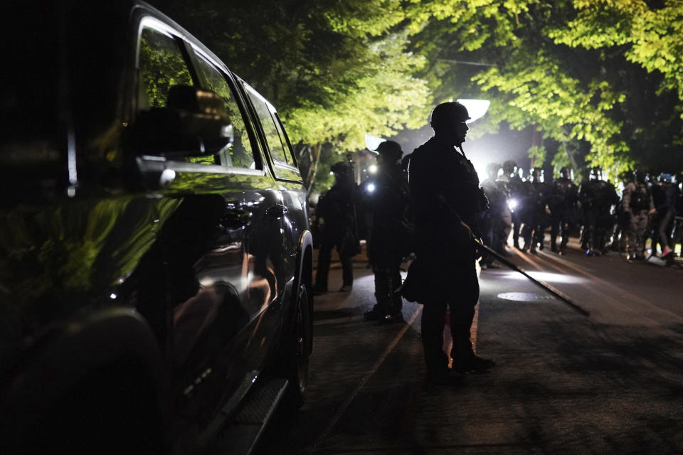 Portland police officers walk through the Laurelhurst neighborhood after dispersing protesters from the Multnomah County Sheriff's Office early in the morning on Saturday, Aug. 8, 2020 in Portland, Ore. (AP Photo/Nathan Howard)