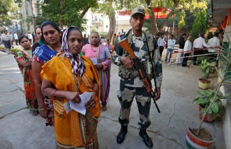 A Border Security Force (BSF) soldier stands guard as women wait to cast their votes at a polling station during the last phase of Gujarat state assembly election on the outskirts of Ahmedabad, India, December 14, 2017. REUTERS/Amit Dave