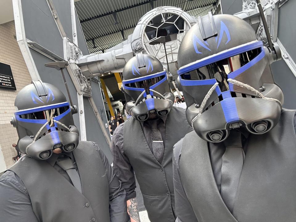 Three men in black shirts, ties and waistcoats wearing black and blue clone trooper helmets.