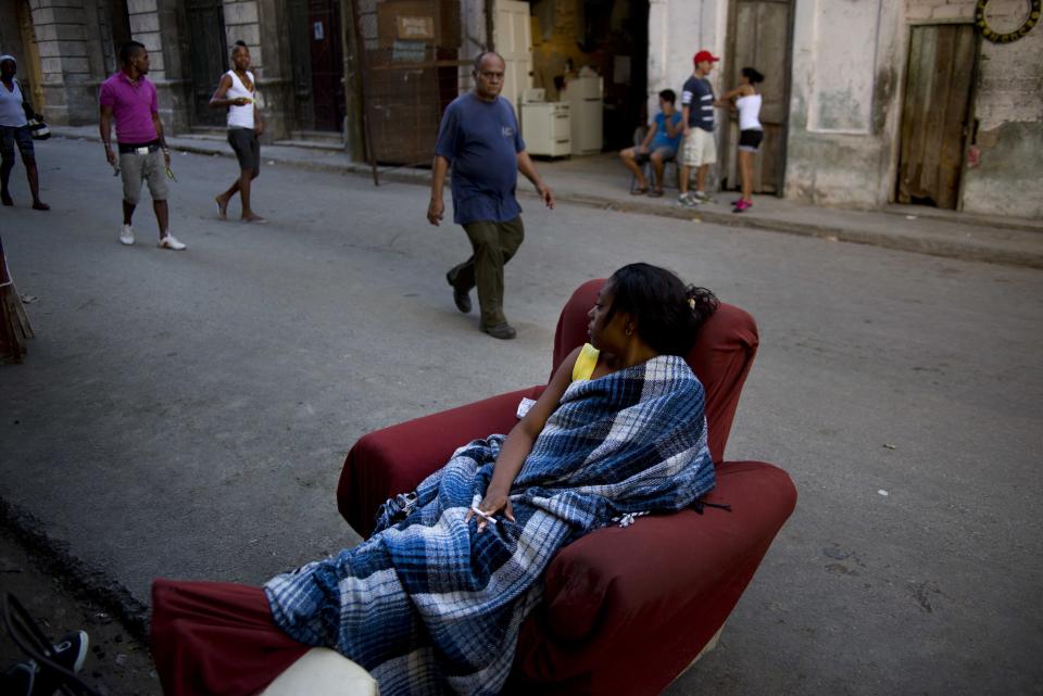 In this March 7, 2014 photo, a woman sitting on a chair waits in a street of Havana, Cuba, to be informed of where she will be relocated after the building where she lived was vacated due to the danger of collapse after the structure failed. Despite reforms in recent years to address the island’s housing problem, such building collapses remain common in Cuba, where decades of neglect and a dearth of new apartments has left untold thousands of islanders living in crowded structures at risk of suddenly falling down. (AP Photo/Ramon Espinosa)