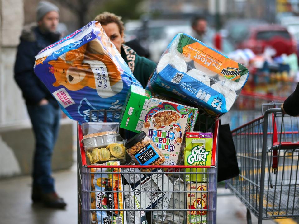 A person is seen behind a shopping cart piled high with goods.