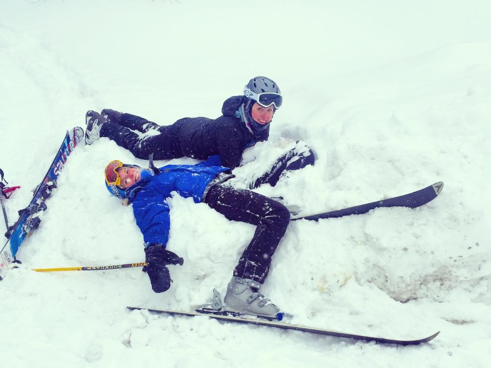 The writer and a friend lying in the snow with snow gear in Vermont