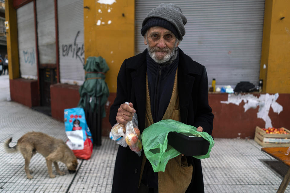 A man poses for a photo holding food he received from a group of neighbors who have formed to help people in need facing hardship amid the new coronavirus pandemic, in the financial district of Montevideo, Uruguay, Saturday, April 25, 2020. (AP Photo/Matilde Campodonico)