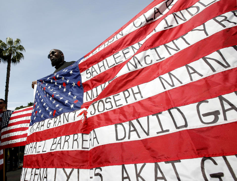 FILE - In this April 8, 2019 file photo, Malaki Seku Amen holds up an American flag with the names of people shot and killed by law enforcement officers, as he and others in rally in support of a bill that would restrict the use of deadly force by police, in Sacramento, Calif. Major police organizations confirmed on May 23, that they won't fight a measure AB392, by Assemblywoman Shirley Weber, D-San Diego that would bar police from using lethal force unless it is necessary to prevent immediate harm to themselves or others. (AP Photo/Rich Pedroncelli, File)