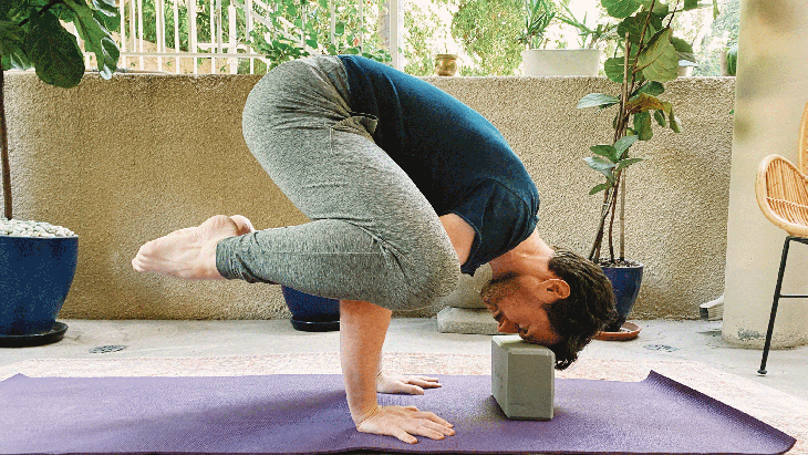Man on yoga mat in Crow Pose with a block underneath his head