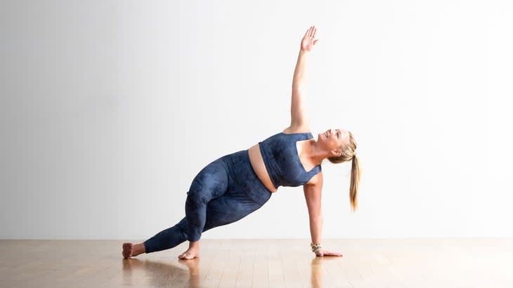 A person demonstrates a variation of Side Plank in yoga, with the top knee bent and foot flat on the ground