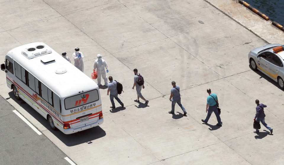 Crew members of a Russian cargo ship take a bus to hospital for their treatment as quarantine officers wearing protective gears stand at the Gamcheon Port in Busan, South Korea, Tuesday, June 23, 2020. South Korea said it was testing more than a hundred workers at the southern port of Busan following a virus outbreak among crew members of a Russian cargo ship. (Cho Jung-ho/Yonhap via AP)