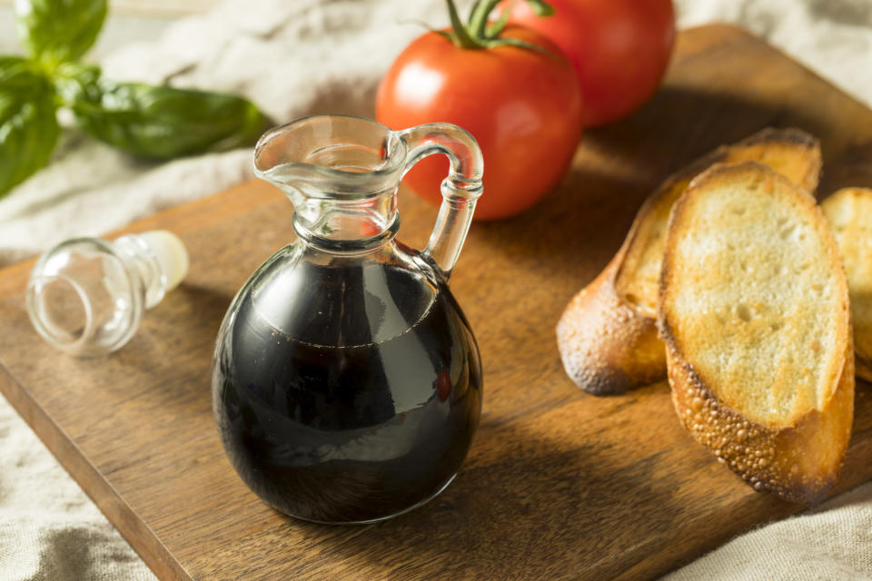 Black Balsamic Vinegar in a Bottle on a wooden board next to bread slices and whole tomatoes