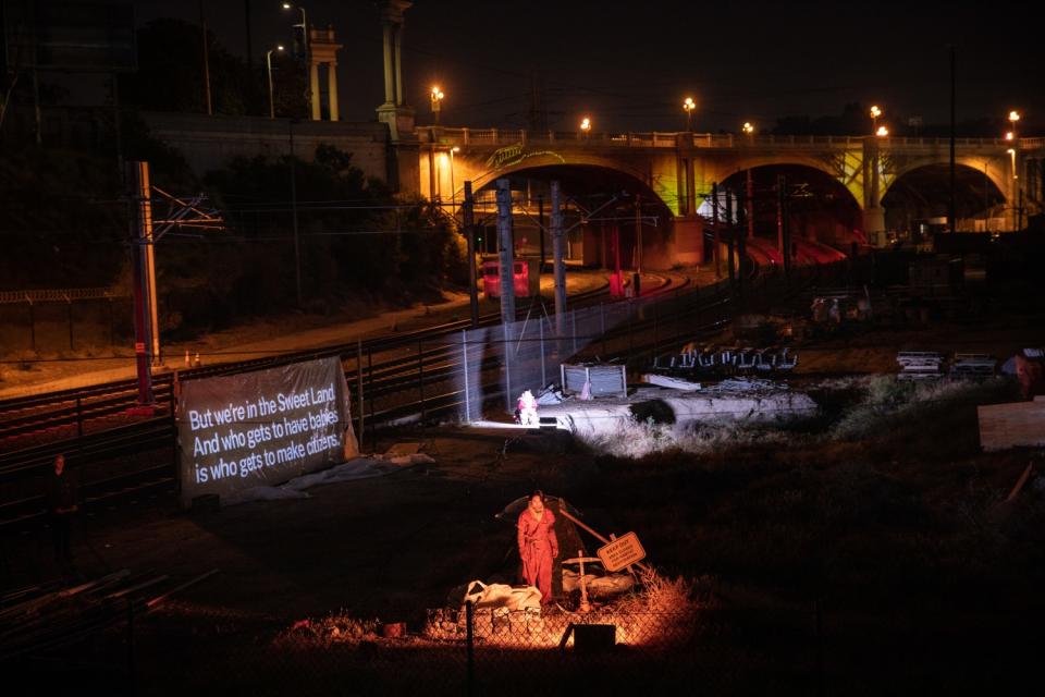 A man stands on a lit stage with a bridge in the background