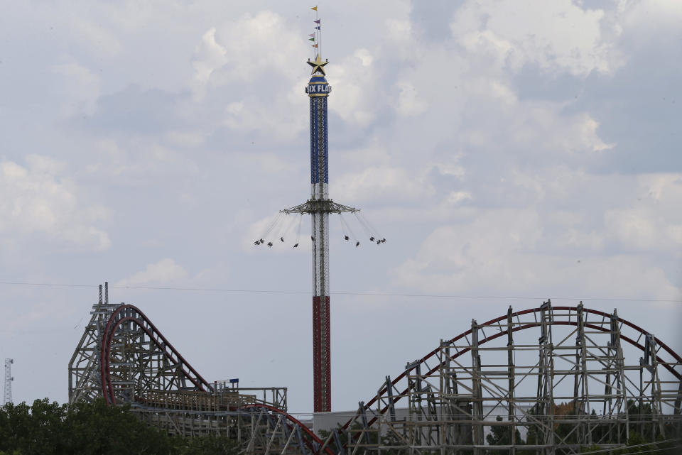 The Texas Giant roller coaster ride sits idle in the foreground as people take in another ride a the Six Flags Over Texas park Saturday, July 20, 2013, in Arlington, Texas. Investigators will try to determine if a woman who died while riding the roller coaster at the amusement park Friday night fell from the ride after some witnesses said she wasn't properly secured.(AP Photo/LM Otero )