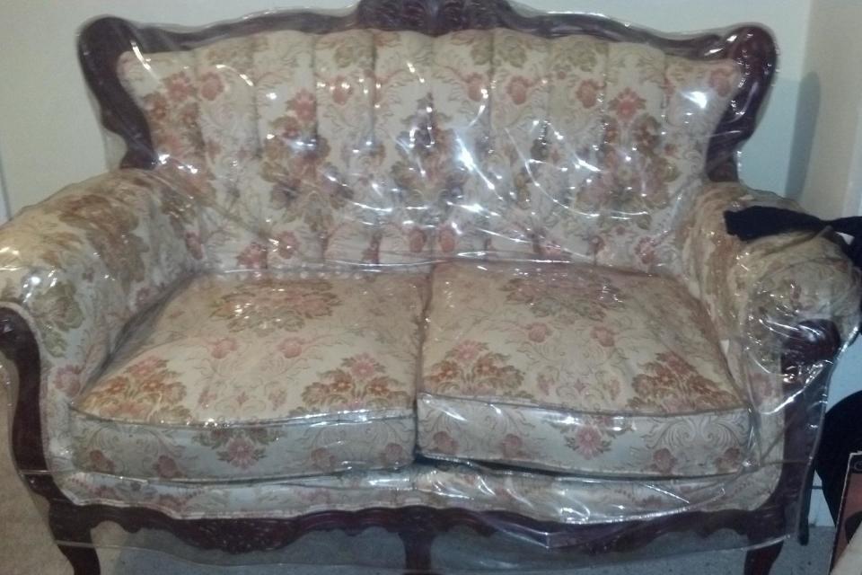 Floral-patterned loveseat with carved wooden trim, covered in a protective plastic cover