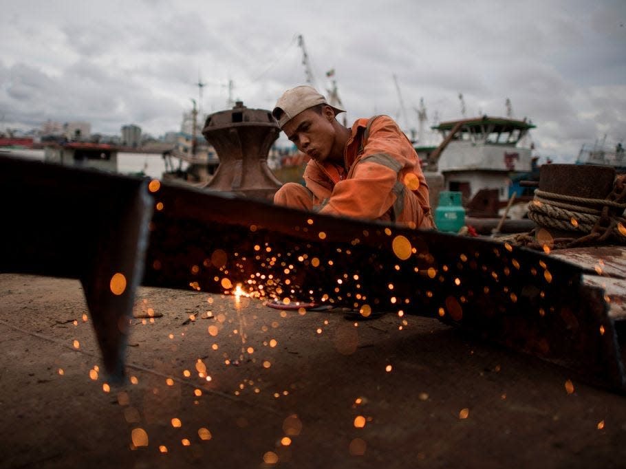 A worker uses a blowtorch to cut metal from a ship at a ship-breaking yard on the bank of the Yangon River in Yangon on May 26, 2018.