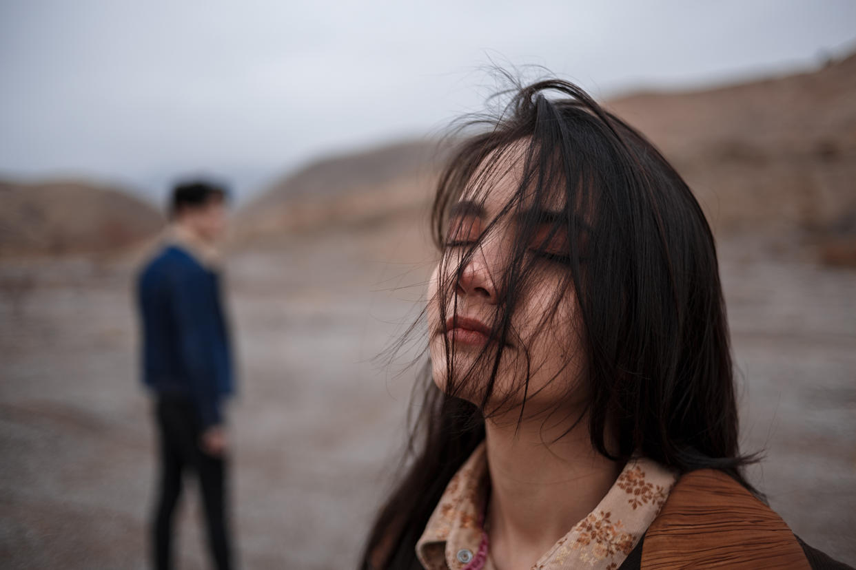 Portrait of a woman in cloudy weather. somewhere behind her, out of focus, is her boyfriend who leaves her after break-up.