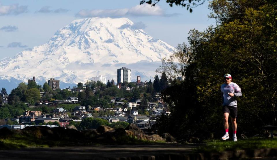 A runner jogs along the Ruston Way Path as Mount Rainier looms through the partly cloudy skies on Wednesday, May 8, 2024, in Tacoma, Wash. Weathers forecasters are predicting rising temperatures into the low 80s this coming weekend.