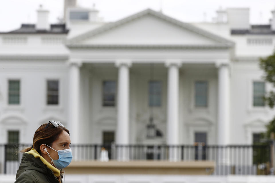 FILE - In this April 1, 2020, file photo a woman wearing a face mask walks past the White House in Washington. Americans are increasingly taking preventative measures, including staying away from large crowds and avoiding touching their hands to their faces, amid growing fears of infection with COVID-19, a new poll from The Associated Press-NORC Center for Public Affairs Research found. (AP Photo/Patrick Semansky, File)