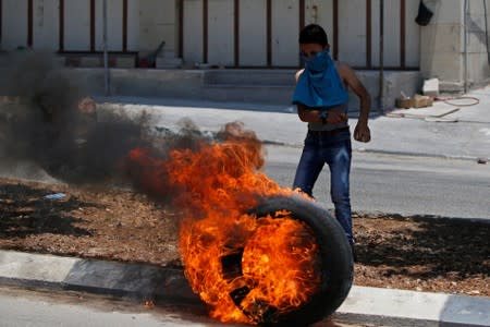 Palestinian boy stands next to a burning tire during clashes with Israeli forces at a protest against Bahrain's workshop for U.S. peace plan, near Hebron, in the Israeli-occupied West Bank