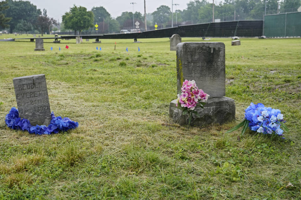 The headstones of Reuben Everett, left, and Eddie Lockard, right, victims of the Tulsa race massacre, are pictured with flowers Monday, May 31, 2021, at Oaklawn Cemetery in Tulsa, Okla., nearly 100 years after the massacre. Fencing has been erected and markers placed in the ground in preparation for the start of mapping, site preparation and excavations of Tulsa race massacre victims in mass graves beginning June 1, 2021. (AP Photo/Sue Ogrocki)