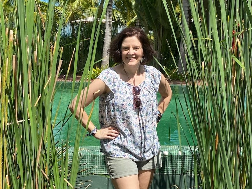 kari becker posing for a photo in a path surrounded by reeds in front of a pool