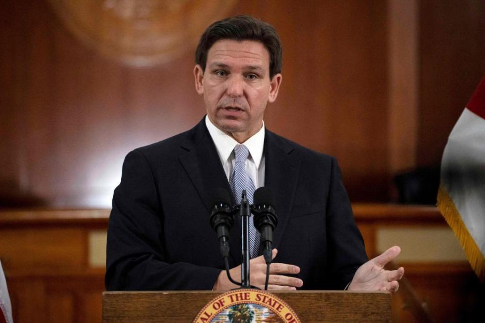 ron desantis speaks behind a microphone while standing at a podium