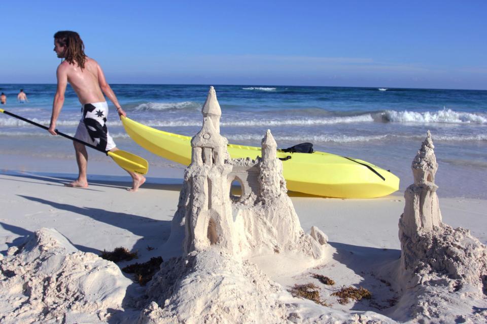In this Jan. 3, 2013 photograph, a man drags a kayak past a sand castle in Tulum, Mexico. Despite its proximity to Cancun and its fellow party neighbor Playa del Carmen, Tulum is not for the same spring break crowd, attracting a mix of bohemians, well-pocketed New Age types and sun-seekers to its turquoise waters and white sandy beaches. (AP Photos/Manuel Valdes)