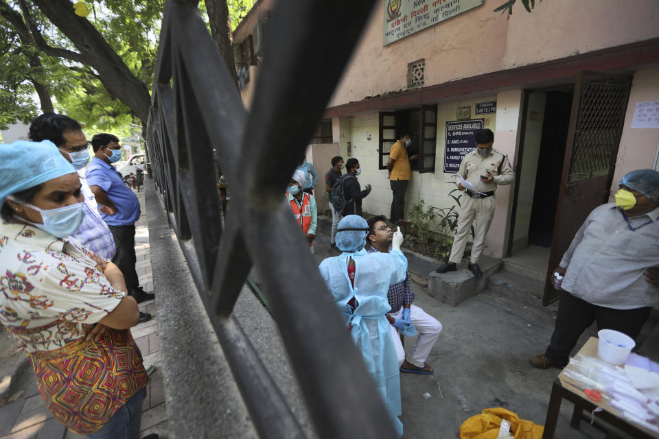 In this Wednesday, June 10, 2020 photo, people look on as health workers take swab test for COVID 19 in New Delhi, India. Two and a half months of nationwide lockdown kept numbers of infections relatively low in India. But with restrictions easing in recent weeks, cases have shot up, raising questions about whether authorities have done enough to avert catastrophe. Half of Delhi’s 8,200 hospital beds dedicated to COVID-19 patients are already full and officials are projecting more than half a million cases in the city alone by July 31. (AP Photo/Manish Swarup)