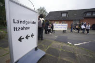 People holding a banner reading "Never again fascism! Never again war!" have gathered next to a signpost reading "Itzehoe Regional Court" in front of the entrance to the China Logistic Center, where the Itzehoe District Court is hearing the trial of a 96-year-old former secretary to the SS commander of the Stutthof concentration campin Itzehoe, Germany, Tuesday, Oct. 19, 2021. The woman is charged of more than 11,000 counts of accessory to murder. Prosecutors argue that the 96-year-old woman was part of the apparatus that helped the Nazi camp function more than 75 years ago. (Markus Brandt/DPA via AP)