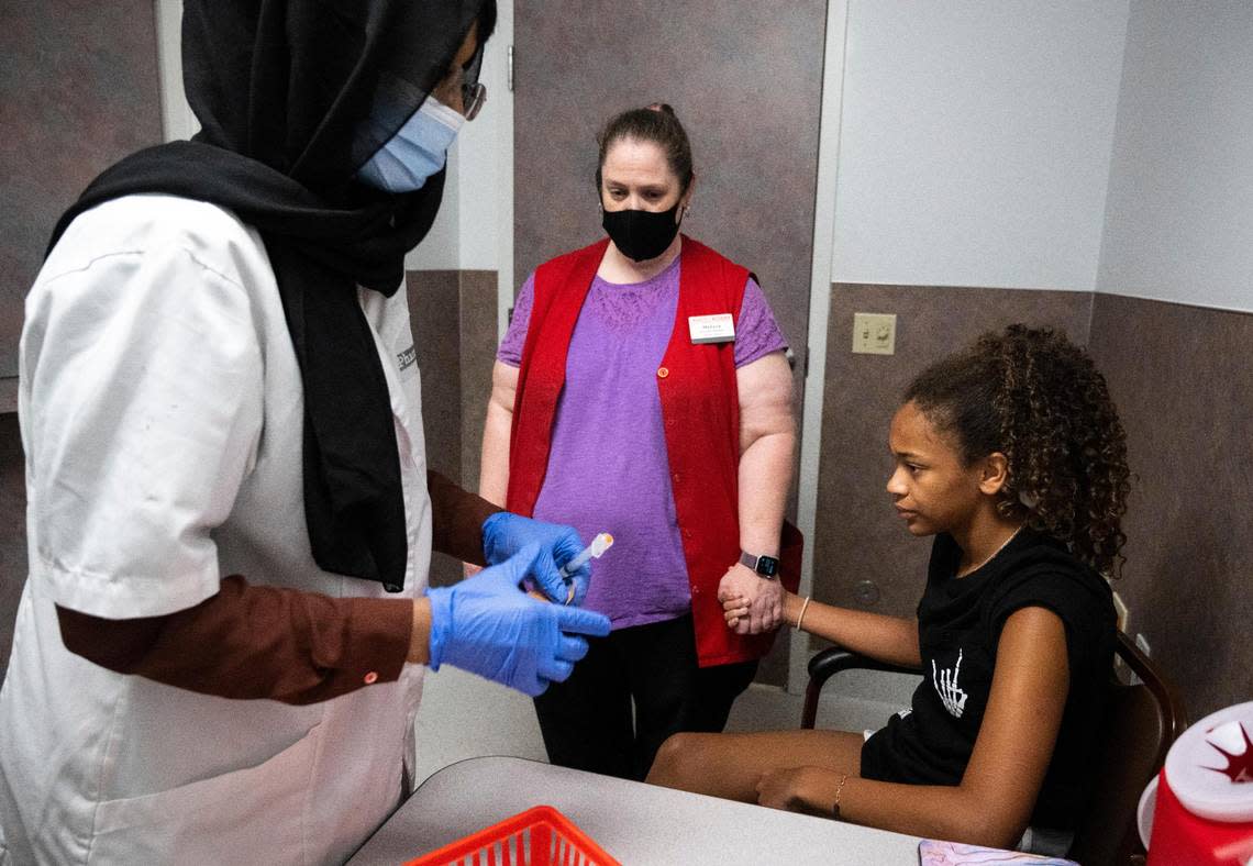 Bartell Drugs head pharmacist Nimo Ahmed, left, prepares to administer a dose of the Pfizer vaccine to Makenzie Porter, 11, right, as she holds her mother, Melissa Porter’s, hand at the store in University Place, on Thursday, July 14, 2022.