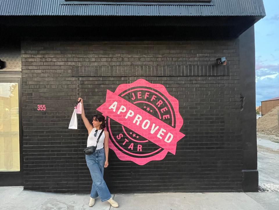 The writer posing with a bag of products next to a pink "Jeffree Star approved" stamp on a black wall
