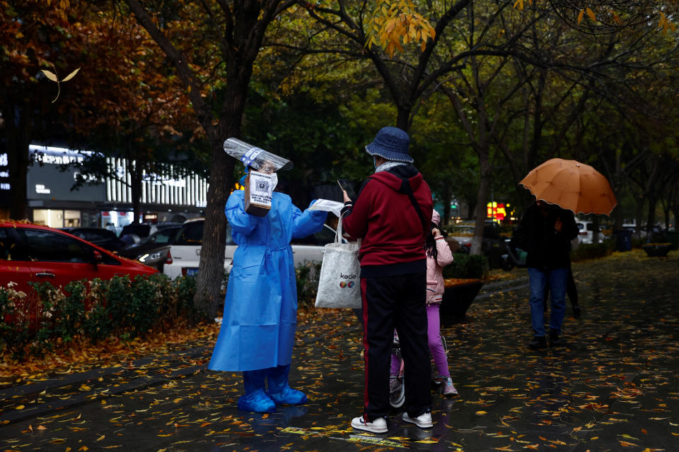 A worker in a protective suit guides people to scan health QR code at a nucleic acid test booth for the coronavirus disease (COVID-19), in Beijing, China November 11, 2022. REUTERS/Tingshu Wang