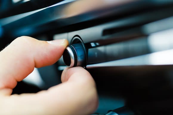 A person turns a knob on a car radio.