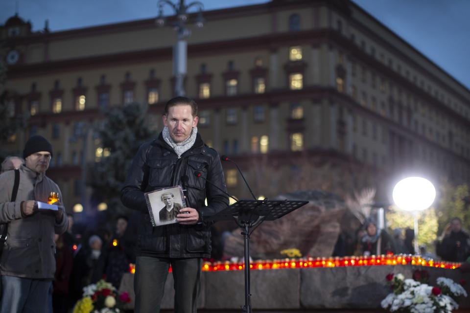 FILE - A man holds portrait of a victim of Soviet-era political repression as other people lay flowers and light candles at a monument in front of the former KGB headquarters in Moscow, Russia, on Oct. 29, 2018, to remember victims of Soviet dictator Josef Stalin. The monument is a large stone from the Solovetsky Islands, where the USSR’s gulag prison system was established. (AP Photo/Alexander Zemlianichenko, File)