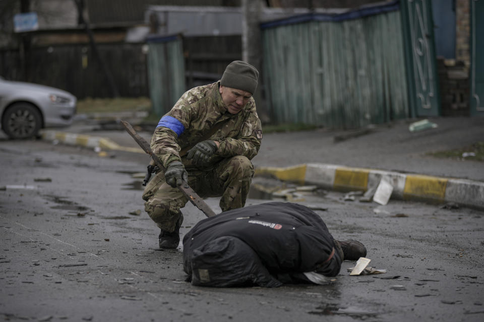 FILE - A Ukrainian serviceman uses a piece of wood to check if the body of a man dressed in civilian clothing is booby-trapped with explosive devices, in the formerly Russian-occupied Kyiv suburb of Bucha, Ukraine, April 2, 2022. On the northwestern fringes of the Ukrainian capital, Bucha had been occupied by Russian forces for about a month, taken as they swept toward Kyiv at the start of the invasion of Ukraine that began in late February 2022. When they withdrew, they left behind scenes of horror. (AP Photo/Vadim Ghirda, File)