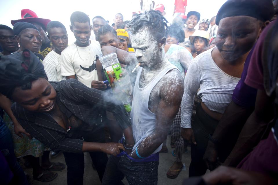 In this Nov. 2, 2018 photo, a voodoo believer who is supposed to be possessed with Gede spirit performs rituals near Baron Samedi's tomb during the annual Voodoo festival Fete Gede at Cite Soleil Cemetery in Port-au-Prince, Haiti. As a proof that they got into trance and their bodies got possessed by Gedes, they drink and wash their faces, their eyes and even their genitals with a mixture of raw rum and hot chili peppers that, according to believers, could burn the skin of any human alive. ( AP Photo/Dieu Nalio Chery)