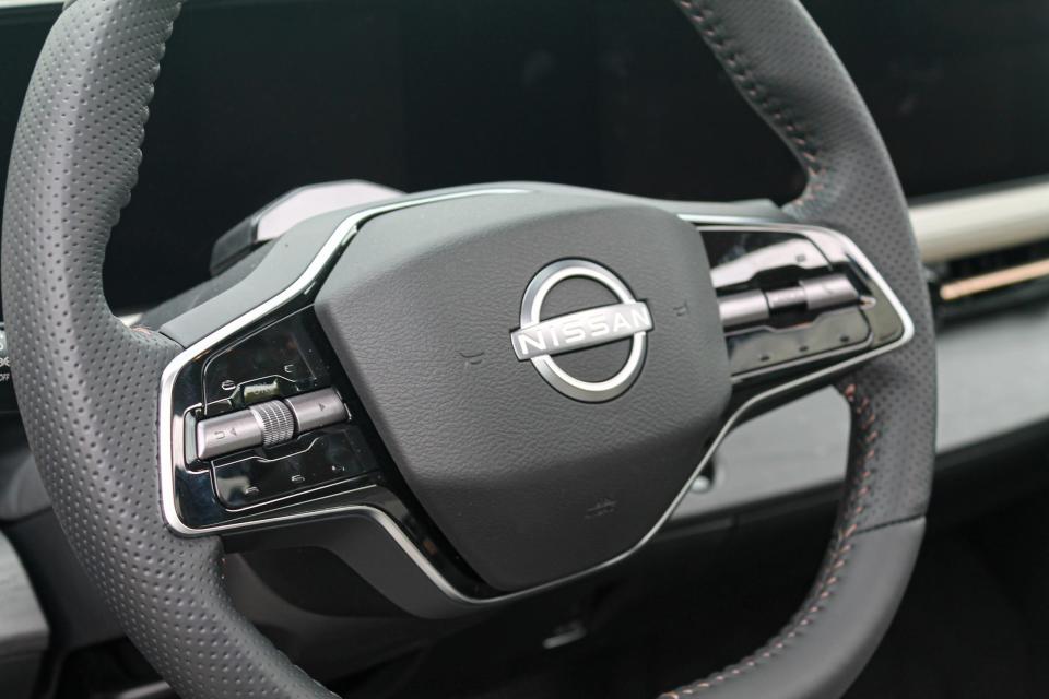 A close-up photograph of the Nissan badge on a steering wheel.