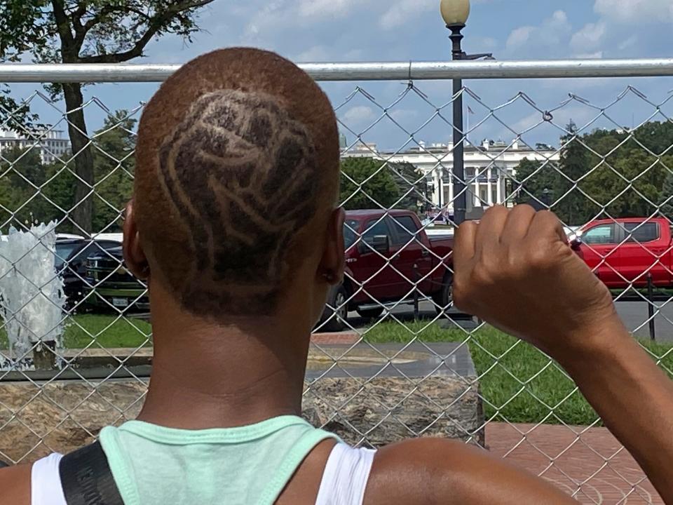 Demetria Hester who had been protesting racial injustice on the streets of Portland, Ore., raises a fist like the one shaved into her head during a trip to Washington, D.C., in August 2020. Hester's hair had been falling out in chunks — from exposure to tear gas, she says — and her voice was cracked and hoarse from leading bullhorn chants for weeks. She had dyed her newly shaved head a golden yellow and shaved the Black Lives Matter fist into the back, tracing it with black dye.