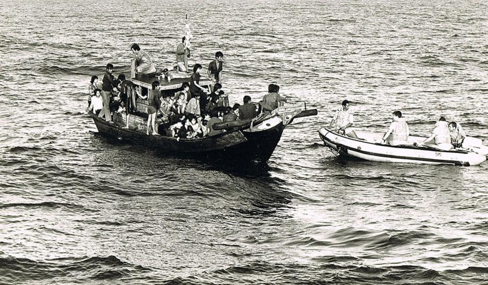 People are seen crammed onto a small boat in a black and white photo.