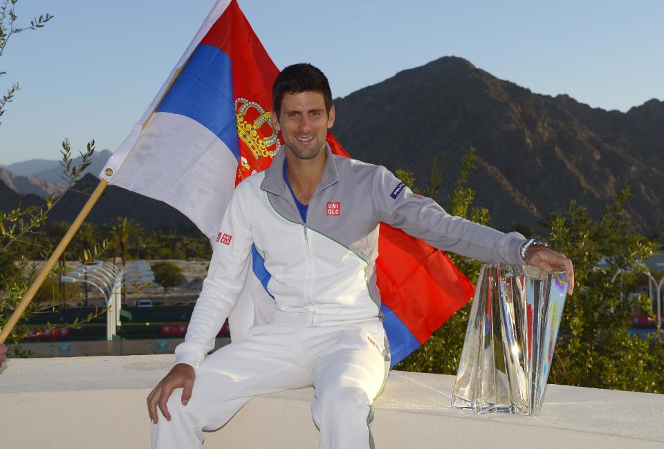 El serbio Novak Djokovic posa entre una bandera de su país y el trofeo que conquistó en el torneo de Indian Wells, California, el domingo 16 de marzo de 2014, tras vencer al suizo Roger Federer (AP Foto/Mark J. Terrill)