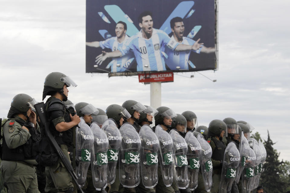 Riot police stand near a billboard with photos of Argentine soccer players Gonzalo Higuain, left, Lionel Messi, center, and Sergio "Kun" Aguero, right, while they monitor a demonstration that blocks the Panamerican highway leading to Buenos Aires, Argentina, on a national strike day, Thursday, April 10, 2014. Opposition unions and political parties called for a national strike to protest raising inflation, low salaries and insecurity.(AP Photo/Victor R. Caivano)