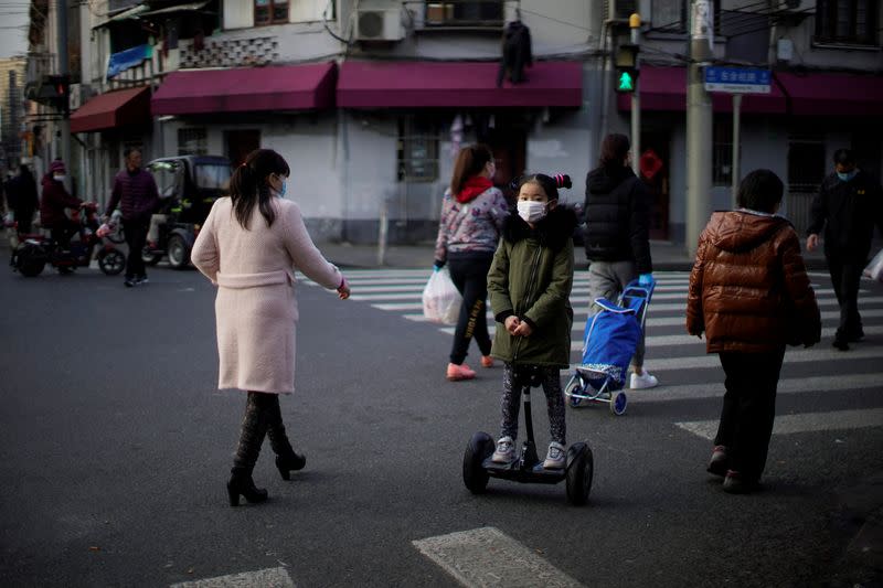 Una niña con una máscara monta un scooter en una calle del centro de Shanghái