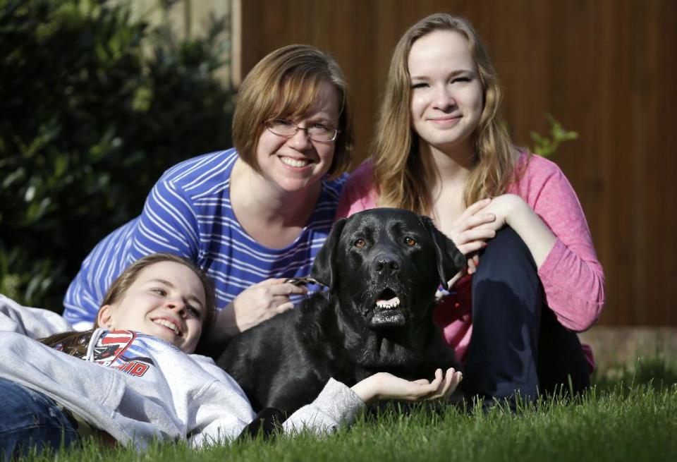 In this photo taken Sunday, April 28, 2013, Kelly Dempsey, center, sits with daughters Jordan, left, and Erin Barker, both 17, and their dog Alou, 9, at their home in Bothell, Wash. In Seattle 10 years ago, a dog named Jeeter became the first professionally trained dog to help a child testify, assisting the twins as they were getting ready to testify against the father they said molested them. Dogs have helped thousands of victims and witnesses since, but some challenges are working their way through the courts, driven by attorneys who claim the dogs are distractions or sympathy magnets. So far, all lower courts have upheld the use of dogs. (AP Photo/Elaine Thompson)