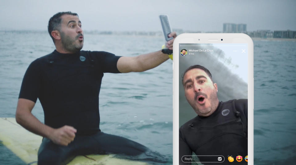 A man on a surfboard filming himself with his phone.
