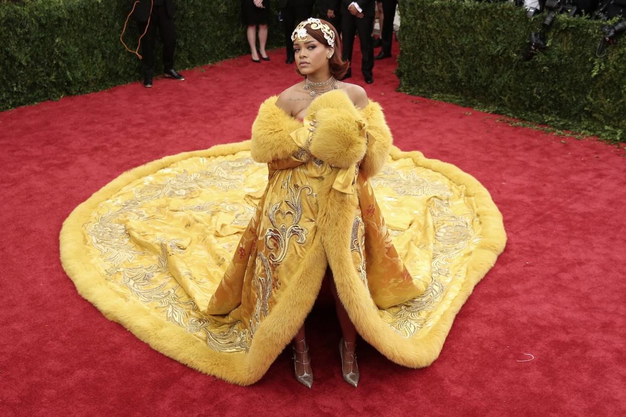 Rihanna's iconic 2015 Met Gala look: A custom yellow coat dress with a large train, fur sleeves, and a gold headpiece.