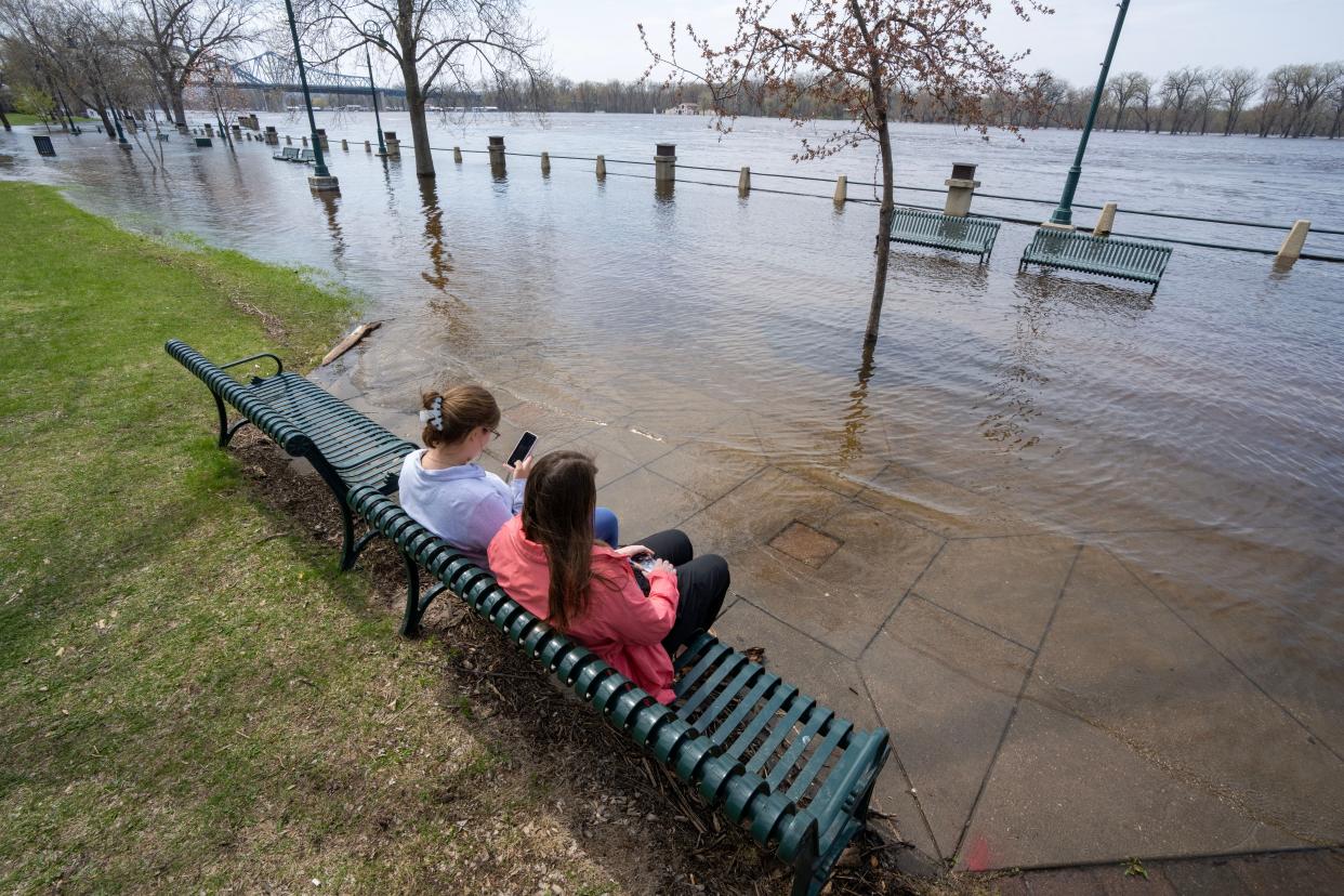 Two women sit on a bench in Riverside Park in La Crosse as the Mississippi River floods up over the banks. In some areas, floods are reaching homes, businesses, farm fields and parks, and covering over roads.