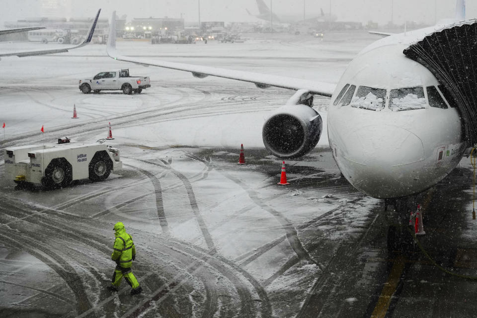 A man walks near a waitig plane as snow falls at John F. Kennedy International Airport Tuesday, Feb. 13, 2024, in New York. Parts of the Northeast were hit Tuesday by a snowstorm that canceled flights and schools and prompted warnings for people to stay off the roads, while some areas that anticipated heavy snow were getting less than that as the weather pattern changed. (AP Photo/Frank Franklin II)